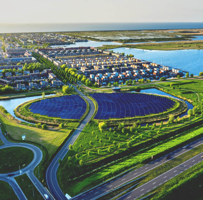Aerial view of a road going through a solar farm and residential area near water.