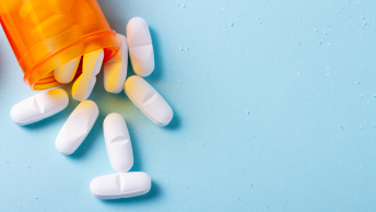 An orange pill bottle laying on its side, spilling white, oblong pills onto a light blue surface