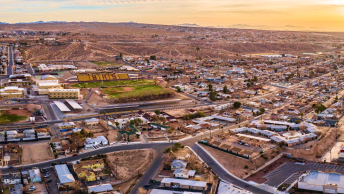 An aerial view of a dry, brown town with roads, buildings, and a green football field in the distance