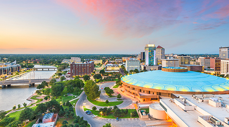 A modern city with bright green park spaces under a color-washed pink and blue sunset sky 