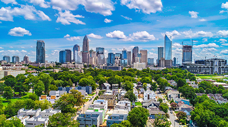 An aerial image of a tree-filled city with towering skyscrapers in the background under a vivid blue sky