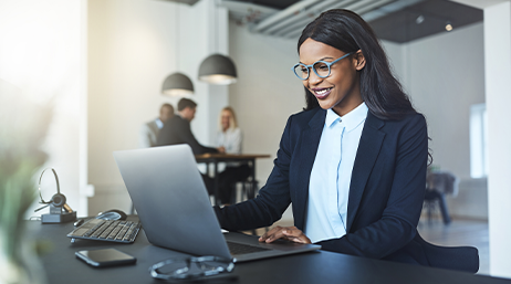 A business professional smiling while working on a laptop at a desk