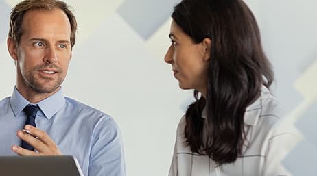 two people having a conversation, with one doing work on a laptop