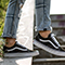 A close-up photo of a pair of feet wearing black and white sneakers standing on concrete stairs beside a lush green planter