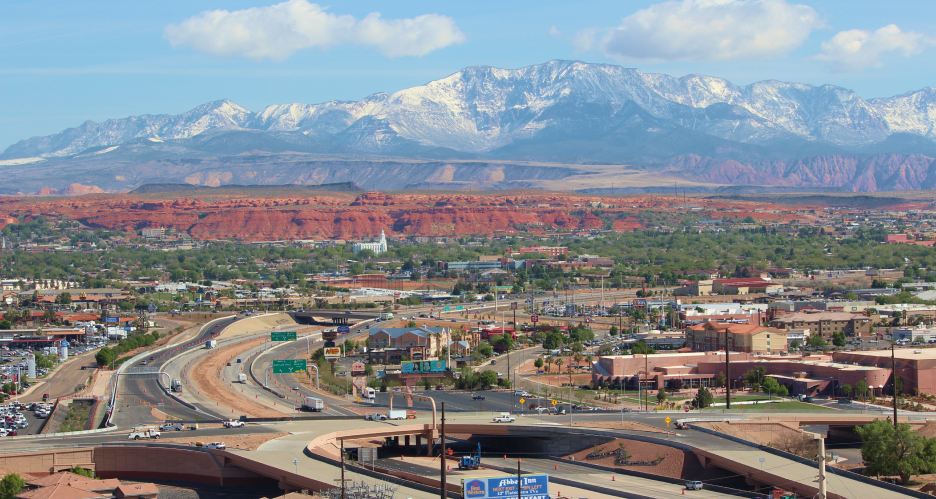 A drone view of Utah’s highway system showing on- and off-ramps in a local town and red and snow-capped mountains